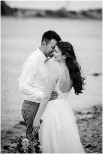 Schwarz weiß Bild eines Brautpaares, di direkt am Wasser stehen und kuscheln