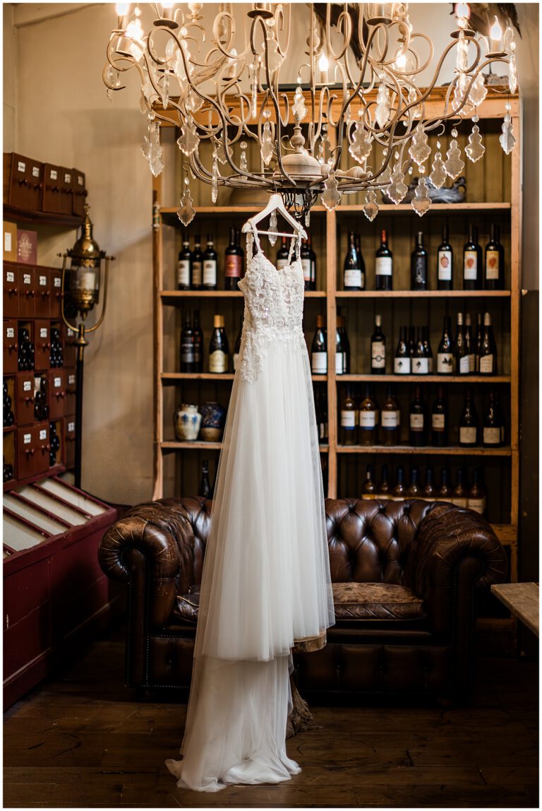 Brautkleid hängt am Kronleuchter im La Dü vor einem Weinregal