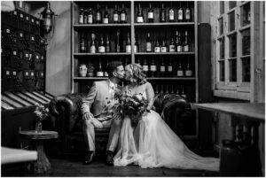 Brautpaar sitzt auf einer Ledercouch vor einem Weinregal im La Dü