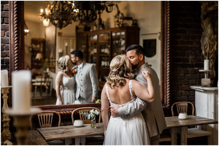 Brautpaar küsst sich auf ihrer Hochzeit vor einem großen Spiegel iim La Dü