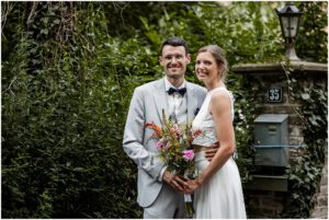 modernes Brautpaar mit Brautstrauß schaut auf dem Kirschhof entspann in die Kamera